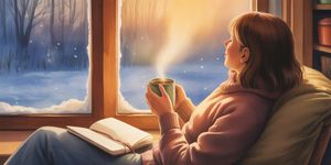 Person sitting peacefully by a window with warm light, journal and tea nearby, snow falling outside